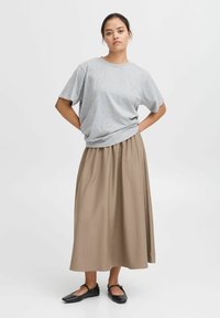 Gray cotton oversized t-shirt with short sleeves, paired with a long beige pleated skirt and black flat shoes. Simple and casual ensemble.