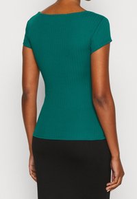 Dopasowany zielony prążkowany top z krótkimi rękawami i szerokim dekoltem, wykonany z elastycznego materiału, w połączeniu z czarnym dołem.