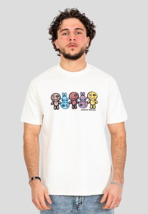 Hombre con pelo rizado y barba lleva una camiseta blanca con dibujos animados coloridos cosidos y texto "WRONG FRIENDS" en la parte delantera.