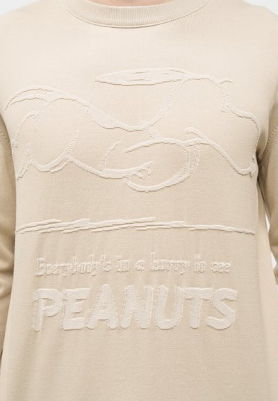 Μπεζ πλεκτό πουλόβερ με ανάγλυφη εικόνα του Σνούπι ξαπλωμένου και κείμενο "Όλοι βιάζονται σε περίπτωση PEANUTS" στο στήθος.