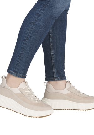 Beige suede sneakers with a white ribbed sole, featuring lace-up design and smooth accents. Worn with dark blue fitted jeans.