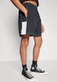 Černé plavky s bílým bočním panelem, elastickým pasem a kontrastním šitím. V kombinaci s černými vysokými teniskami.