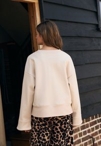 Beige oversized sweatshirt met afgezakte schouders, geribbelde boorden en een brede hals, gecombineerd met fluwelen broek met luipaardprint.