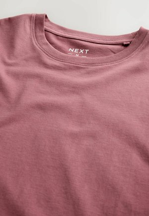 Camiseta de algodón de corte normal y manga corta en color rosa empolvado, con una textura suave y la etiqueta "NEXT" impresa en el escote.