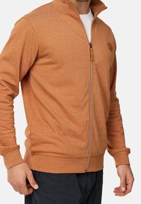 Veste zippée orange en tissu texturé à rayures. Dotée d'un col haut, de poignets côtelés et d'une accent logo sur la poitrine.