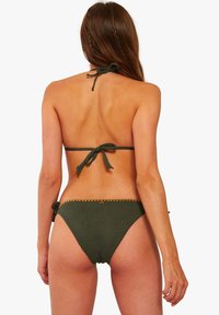 Set bikini verde oliva realizzato in un tessuto texturizzato, con top a halter con allacciatura sul retro e laccetti regolabili sui fianchi, accentuato da bordi a onde.
