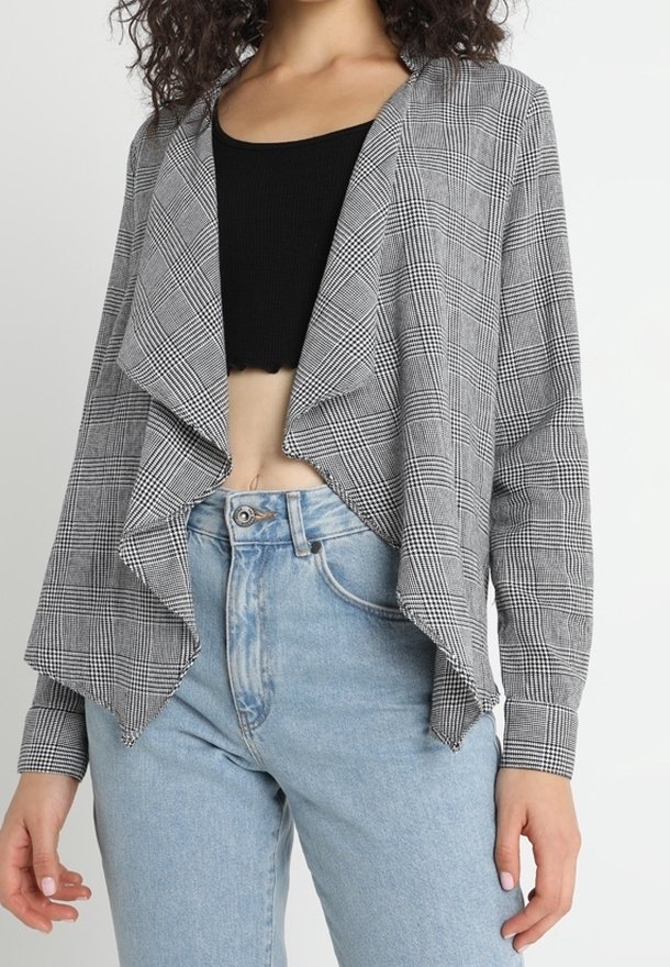 Cardigan à carreaux noir et blanc à ouverture devant avec un col drapé, tissu léger, manches longues et coupe décontractée portée sur un haut ajusté.