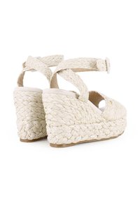 Sandalias de cuña con un upper trenzado de fibra natural en beige claro, diseño de punta abierta con correas en el tobillo y una suela de cuerda texturizada.