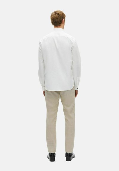 Witte overhemd met lange mouwen, gecombineerd met lichtbeige pantalon. Zachte textuur; minimalistisch ontwerp zonder zichtbare patronen. Zwarte schoenen.