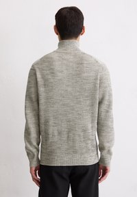 Helles graues, geripptes Sweatshirt mit hohem Kragen, langen Ärmeln und strukturiertem Finish, kombiniert mit dunklen Hosen. Ansicht von hinten.