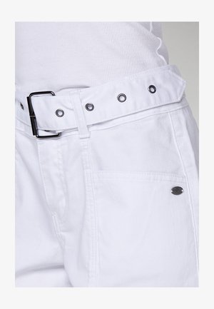 Bílé kalhoty z bavlny se širokým pasem, černou kovovou sponou a stříbrnými očky. Obsahují boční kapsy a detail s logem.