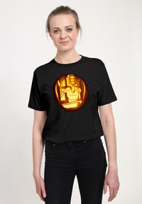 Czarna bawełniana koszulka z krótkim rękawem, z okrągłym pomarańczowym wzorem dyni z stylizowaną twarzą na środku. Luźny krój.