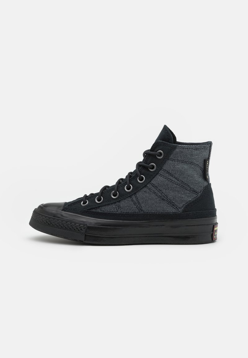 Baskets montantes noires et gris foncé avec semelle en caoutchouc noire, bout renforcé, œillets métalliques et fermeture à lacets, vues de côté extérieur.