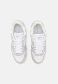 Zapatillas Lacoste con parte superior de cuero gris y blanco, puntera perforada y cordones blancos. Marca destacada en la lengüeta y el costado.