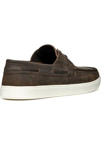 Zapato de cuero marrón con un diseño de corte bajo, que presenta una punta redondeada, suela de goma blanca y acentos de costura en contraste.