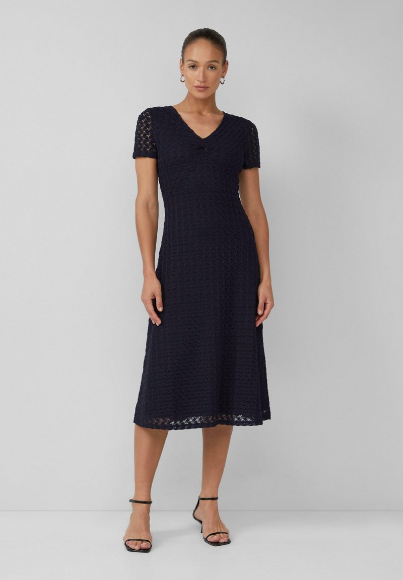 Robe midi en dentelle bleu marine avec des manches courtes, un décolleté en V, un corsage ajusté et une jupe évasée. Motif texturé et taille bien marquée.