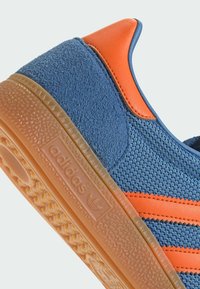 Blue textile sneaker with orange accents, textured surface, and rubber gum sole. Features three side stripes and an embossed logo on the sole.