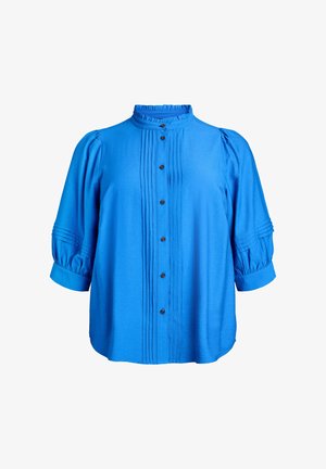 Plava košulja na kopčanje s naboranim prednjim dijelom, visokim izrezom i naduvenim rukavima s manžetnama na krajevima. Izrađena od glatkog, laganog tkanja.