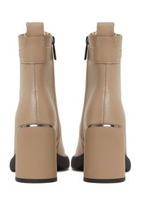 Paire de bottines beiges à talons blocs, fermeture éclair à l’arrière et garniture métallique au-dessus du talon, vue de dos.