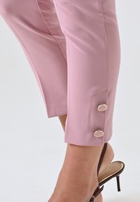 Pantaloni aderenti rosa con una texture liscia, lunghezza croppata e due bottoni circolari dorati per accentuare l'orlo.