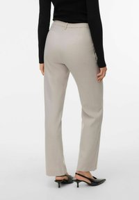 Lysebeige skreddersydde bukser med rette ben, en glatt tekstur og enkelt midjebånd. Kombinert med svarte høyhælte slingbacks.