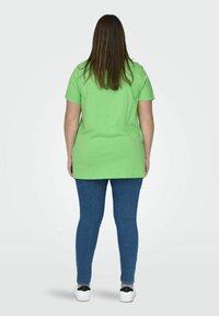 Zöld pamut póló rövid ujjakkal, kék farmer skinny jeans-szel és fehér sportcipőkkel párosítva, hátulról nézve.