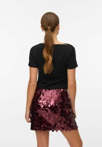 Črna kratka majica s kratkimi rokavi v kombinaciji z bleščečo, okrašeno krilom v odtenkih burgundca, ki ima raven kroj in rob s valovitimi robovi.