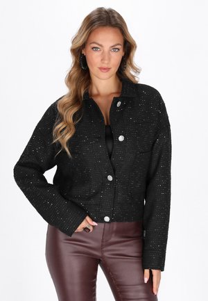 Giacca corta nera in tessuto strutturato, adornata con scintille argentate e decorata con due bottoni ornamentali. Abbinata a pantaloni bordeaux.