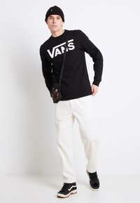 Czarna bluza z białym logo "VANS", jasne spodnie, czarno-białe buty oraz mała czarna torba z detalem w panterkę.