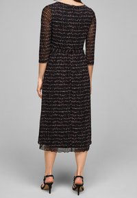 Vestido negro hasta la rodilla con mangas 3/4 semitransparentes, que presenta un patrón texturizado de formas blancas y cobre, y una cintura ajustada.