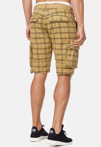 Cargo shorts in a light brown plaid pattern with multiple pockets, a textured fabric, and stitched detailing at the seams.