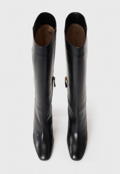 Black knee-high leather boots with a sleek design, featuring a square toe and gold hardware accents on the side zippers. Smooth texture.