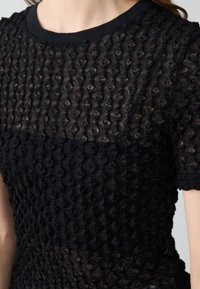 Top nero con texture caratterizzato da un design a maglia con modelli circolari in rilievo. Scollo a coste e maniche corte. Sezioni trasparenti che rivelano una diversa opacità.
