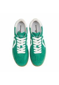 Baskets en suède vert avec des lacets et des accents blancs, présentant une forme arrondie et une semelle en caoutchouc. Logo imprimé à l'intérieur de la chaussure.