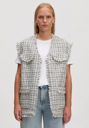 Tweed-Weste mit fransigen Kanten, hellgrauem und weißem Karomuster, offener Vorderseite und zwei vorderen Taschen, getragen über einem weißen T-Shirt.