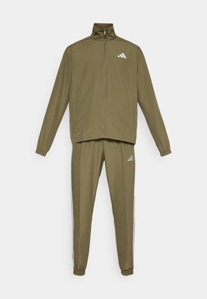 Olíva zöld sportöltözet, amely zipzáros dzsekiből és hozzá illő nadrágból áll, rugalmas mandzsetta, oldalsó zsebek és logó részletek találhatók rajta.