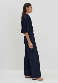 Dark denim outfit featuring a short-sleeve top with a stand collar, wide-leg pants, and contrasting yellow stitching.