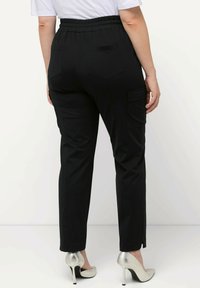Pantaloni neri a sigaretta con vita elastica, tasche laterali e una texture liscia. Abbinati a scarpe con tacco alto argentate.