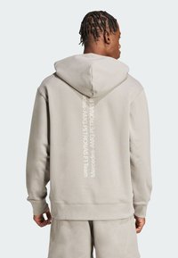 Beige hoodie med dragsko och vertikal vit text på baksidan. Mjuk tyg med avslappnad passform och ribbade ärmmuddar.