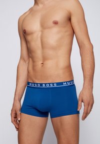 Blaue Baumwoll-Boxershorts mit weißem, gebrandetem Bund. Der Stoff wirkt glatt und dehnbar und bietet eine enganliegende Passform.