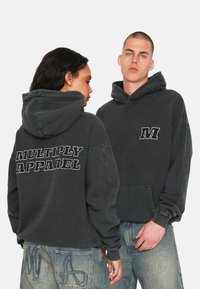 Uhlová mikina s kapucí a přední kapsou, s bílým vyšitým "M" na hrudi a nápisem "MULTIPLY APPAREL" na zadní straně. Bavlněný materiál, volný střih.