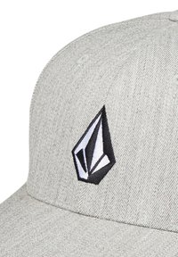 Grijze pet van textuurstof met een zwart-wit geometrisch logopatch op de voorkant. Gebogen klep en gestikte details aanwezig.