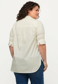 Hellbeige Knopfhemd aus weichem Stoff, mit kurzen Puffärmeln und Seitenschlitzen. Es hat einen lockeren Schnitt und eine geraffte Rückendetails.