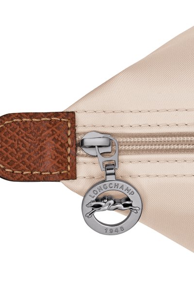 Beige fabric with brown leather tab stitched near silver zipper pull featuring Longchamp logo and horse emblem, dated 1948.