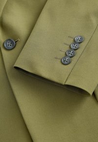 Olivezielenowa marynarka z gładkiego materiału. Posiada cztery szare guziki na mankietach, z srebrnymi przeszyciami.