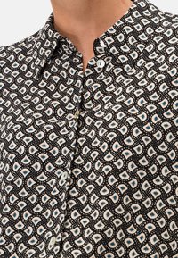 Camicia nera con bottoni, caratterizzata da un motivo paisley in bianco e azzurro chiaro, con una texture morbida e dettaglio del colletto arrotondato.