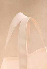 Canvas-Tasche mit doppelten flachen Griffen in hellbeige, die eine glatte Textur und klare Linien aufweist und ihr minimalistisches Design hervorhebt.