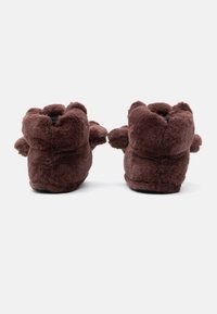 Smeđe plišaste papuče s krznenom teksturom, zaobljenog oblika i podignutim detaljima sa strane, s jednostavnim dizajnom koji se navlači.