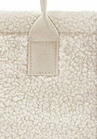 Primo piano di un tessuto in pile beige con un dettaglio a scelta rettangolare cucito, realizzato in materiale tessuto liscio.