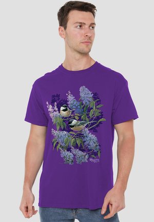 Lila Baumwoll-T-Shirt mit einem floralen und Vogel-Druck in lebendigen Farben, das zwei Vögel zwischen lila Blumen und grünen Blättern zeigt.